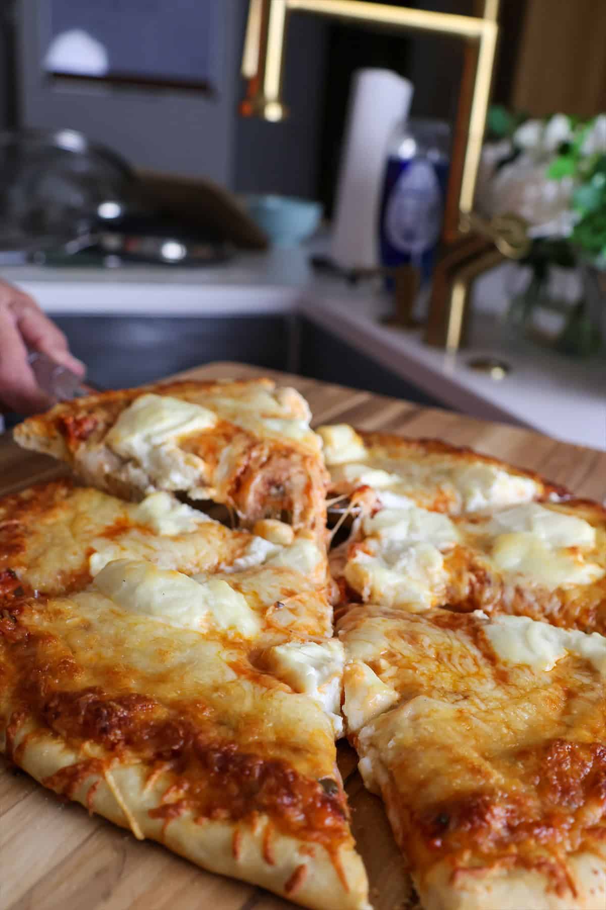 Sliced smoked three cheese pizza on a wooden cutting board with golden brown crust and dollops of ricotta.