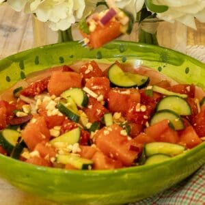 Watermelon feta salad in a green watermelon bowl with a fork lifting a bite of melon, feta, and red onion.