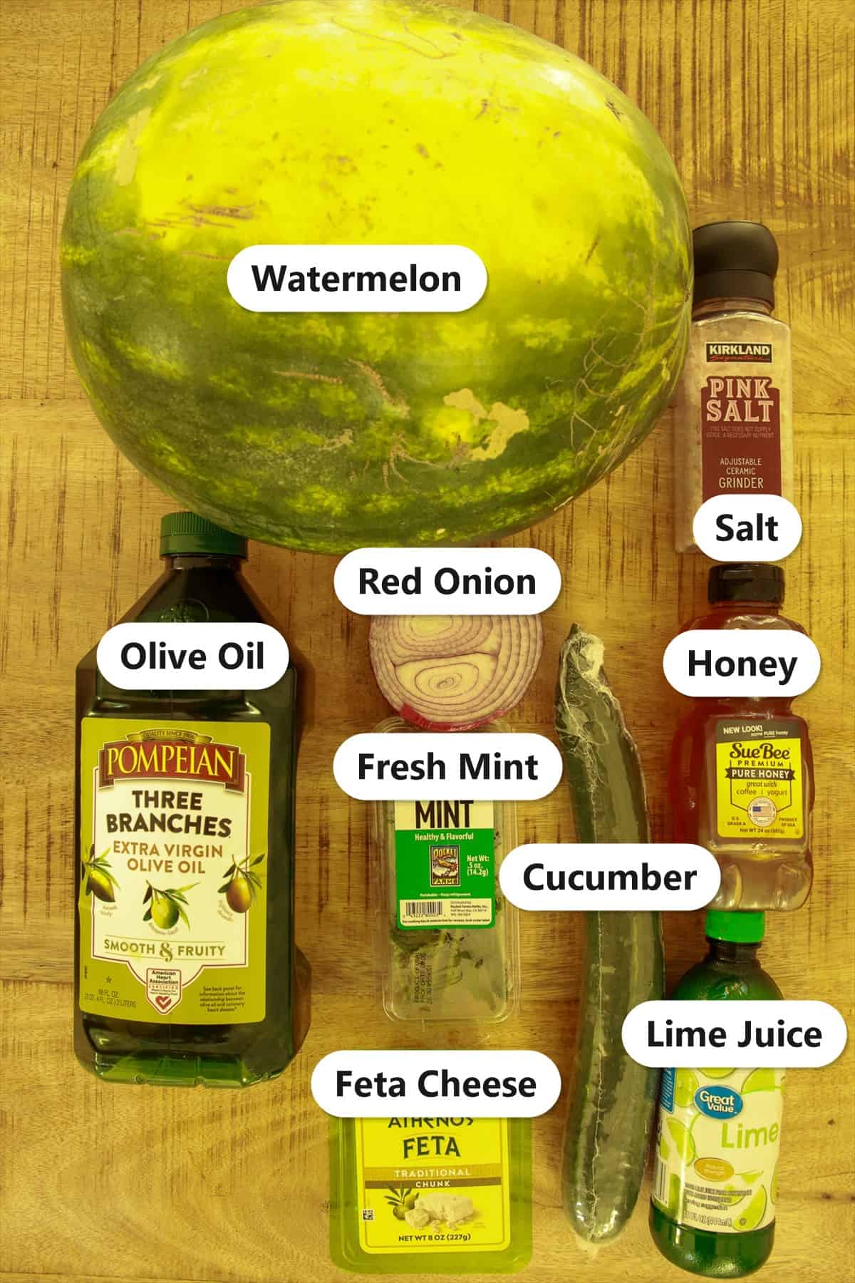 Labeled ingredients for watermelon feta salad including watermelon, cucumber, feta cheese, fresh mint, red onion, honey, lime juice, olive oil, and salt.