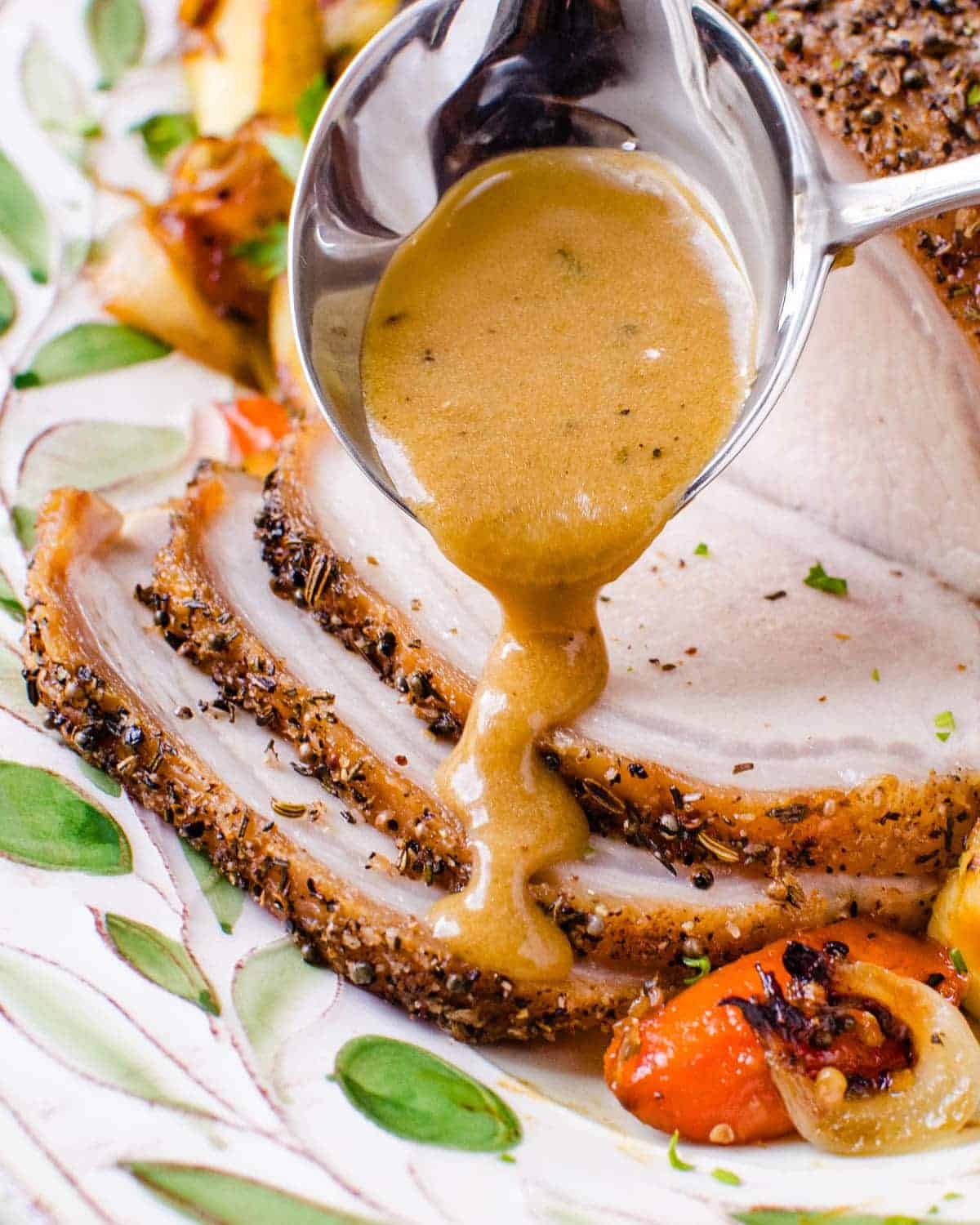 Sliced herb crusted pork loin roast with pan gravy poured from a spoon over the slices.