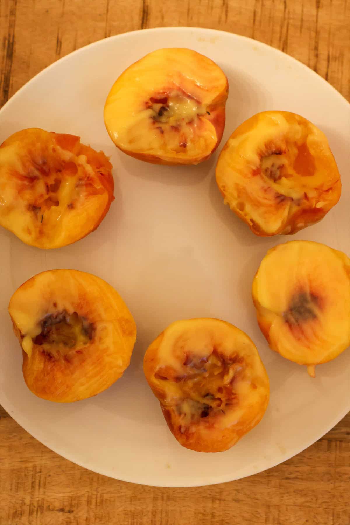 Halved and pitted peaches brushed with melted butter on a white plate, ready for the grill.