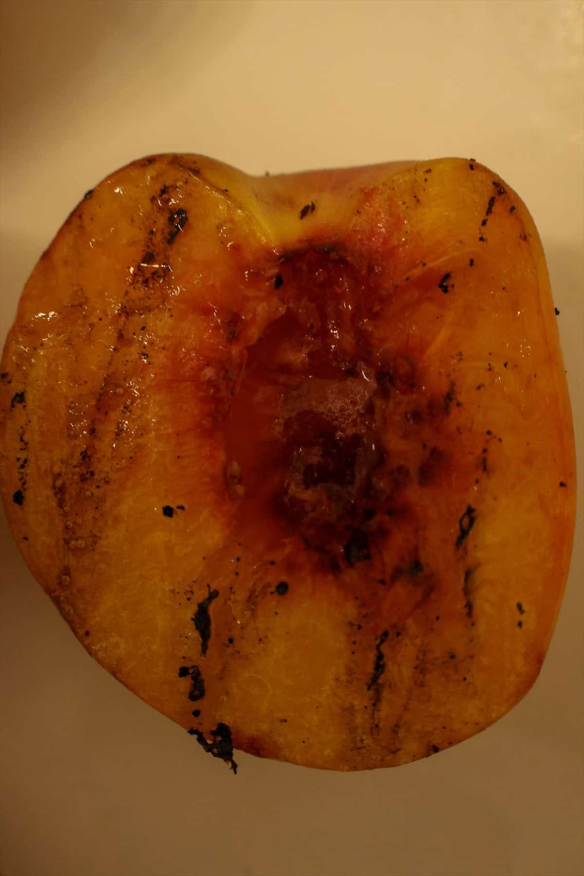 Close up of a grilled peach half with dark caramelized grill marks on the cut side.