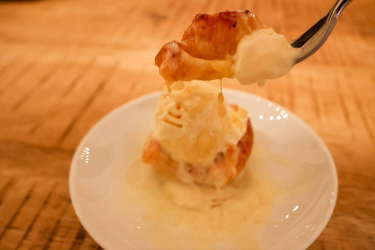 Spoonful of warm grilled peaches with melting vanilla ice cream lifted from a white dessert plate.