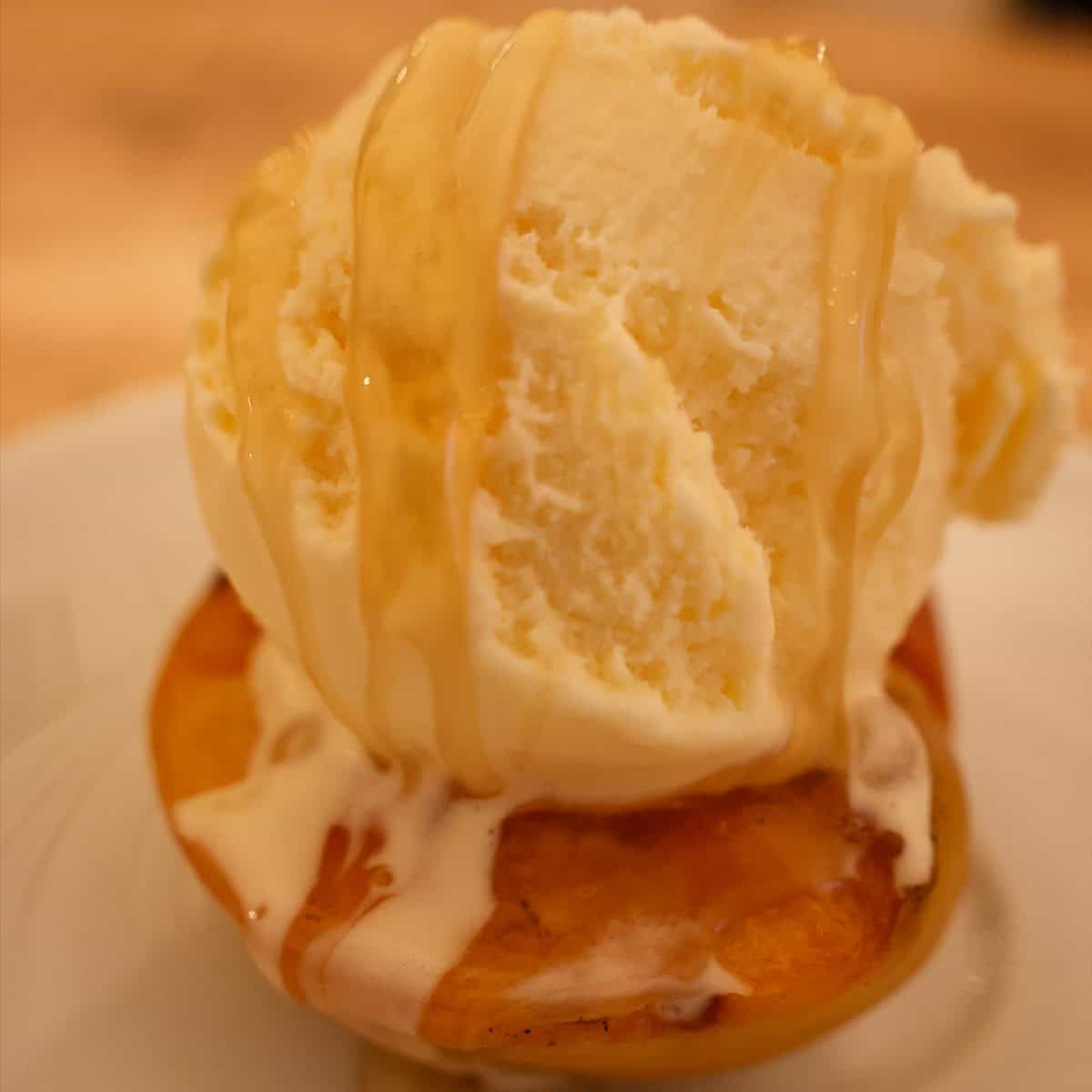 Grilled peach half topped with a scoop of vanilla ice cream and a drizzle of honey on a white plate.