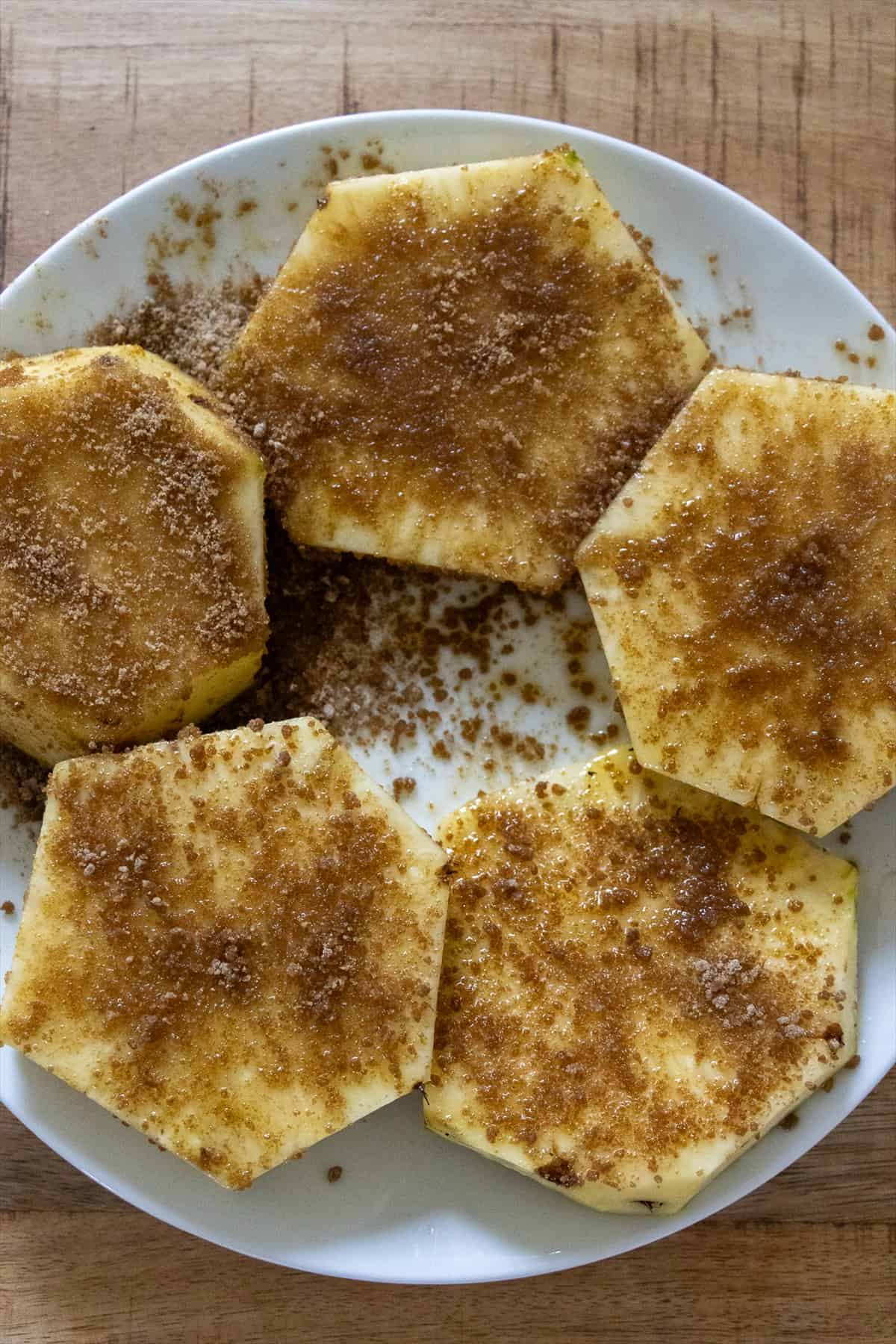 Pineapple rings brushed with melted butter and sprinkled with brown sugar on a white plate.