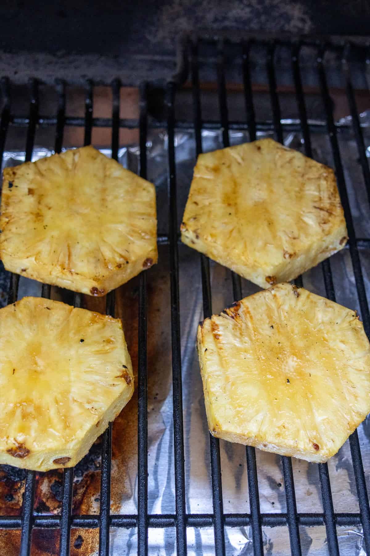 Pineapple rings cooking in a single layer on hot grill grates.