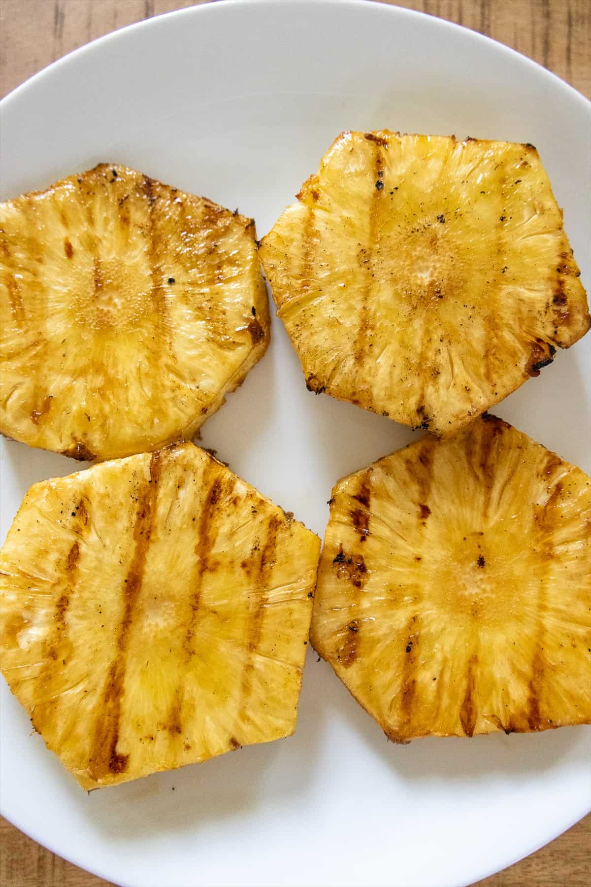 Grilled pineapple rings with golden char marks resting on a white plate.