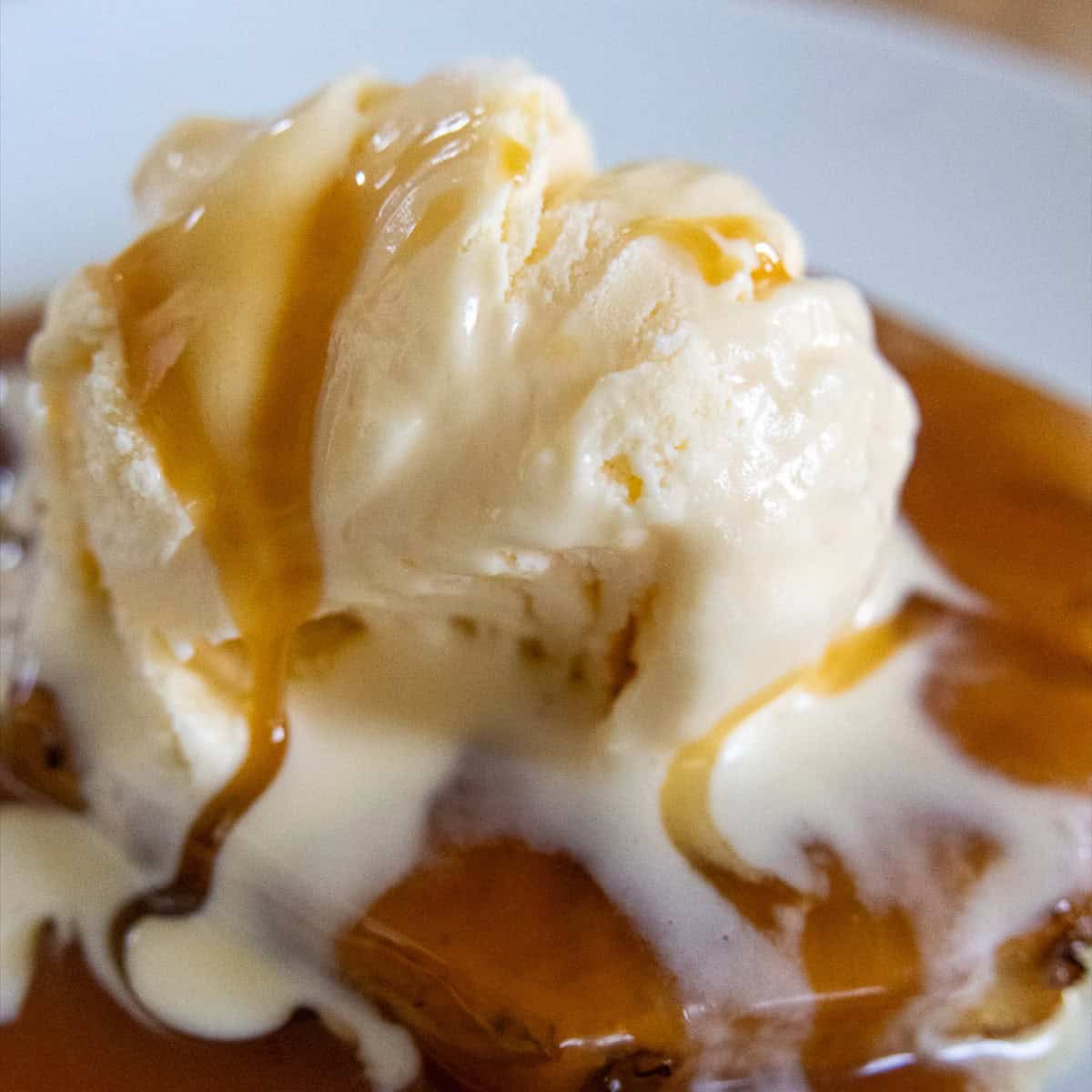 Scoop of vanilla ice cream melting over a grilled pineapple ring with caramel sauce drizzled on top.