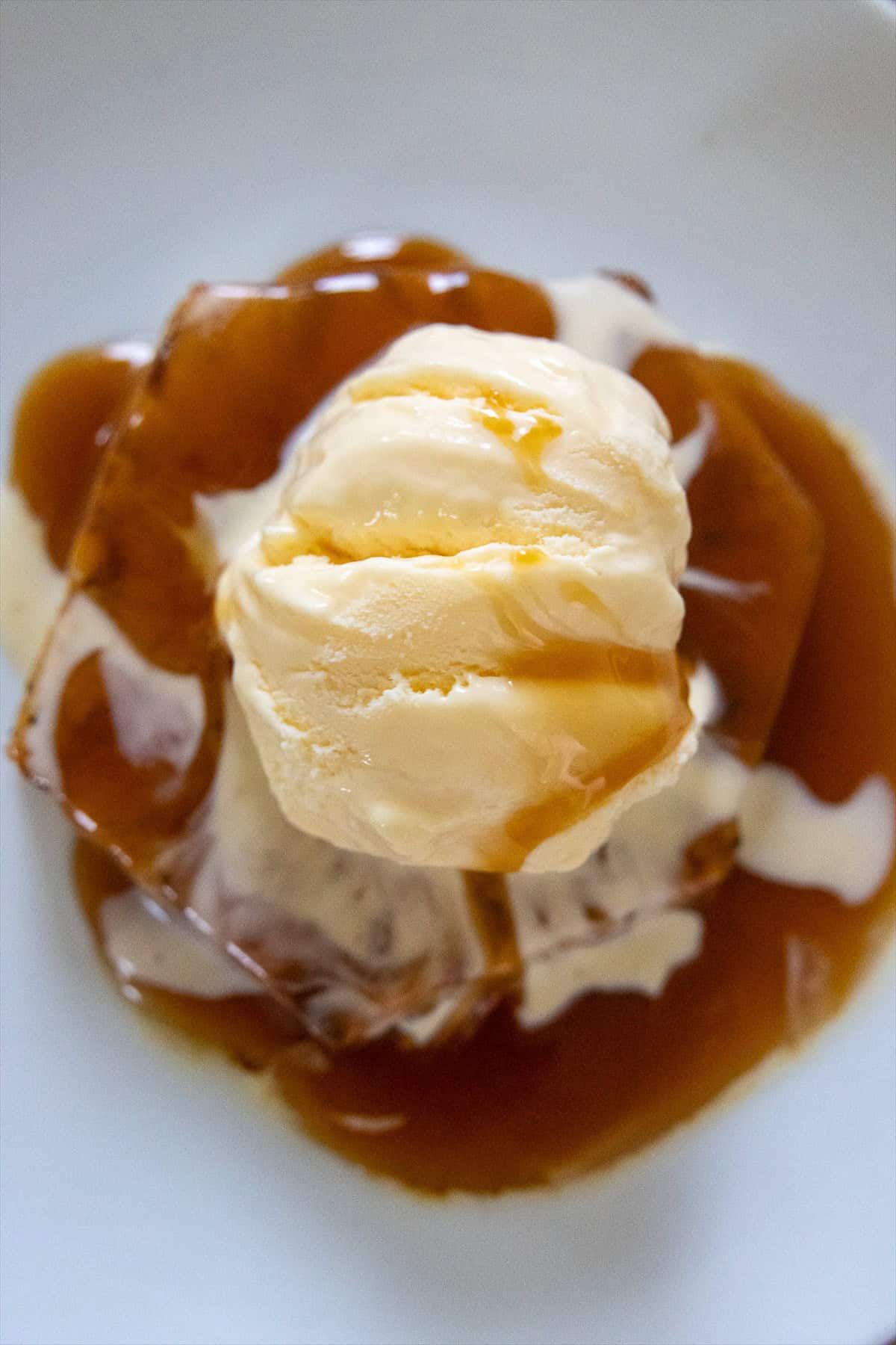 Grilled pineapple sundae on a white plate with vanilla ice cream and a pool of warm caramel sauce.