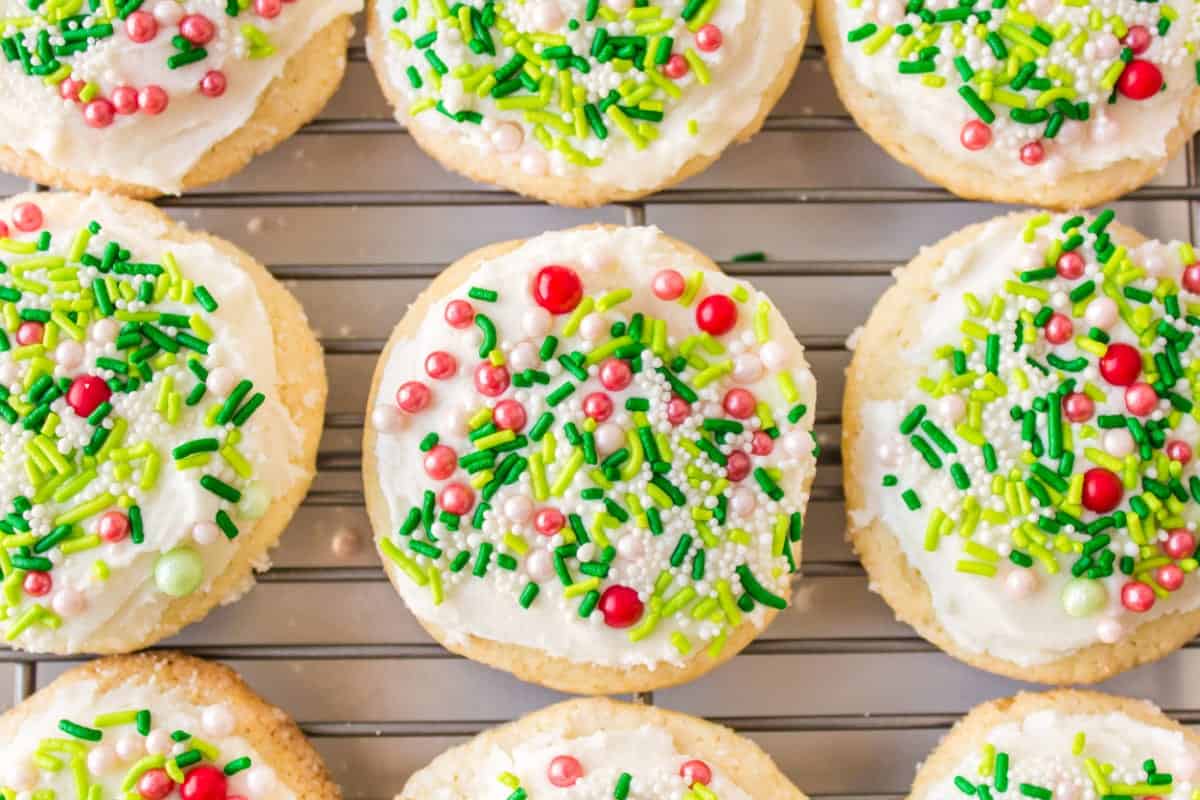 Soft frosted Christmas Lofthouse cookies topped with white frosting and red and green sprinkles on a cooling rack.