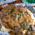 Slow cooker pork chops smothered in creamy mushroom gravy over mashed potatoes on a blue and white plate.