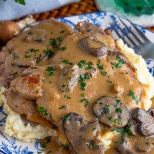Slow cooker pork chops smothered in creamy mushroom gravy over mashed potatoes on a blue and white plate.