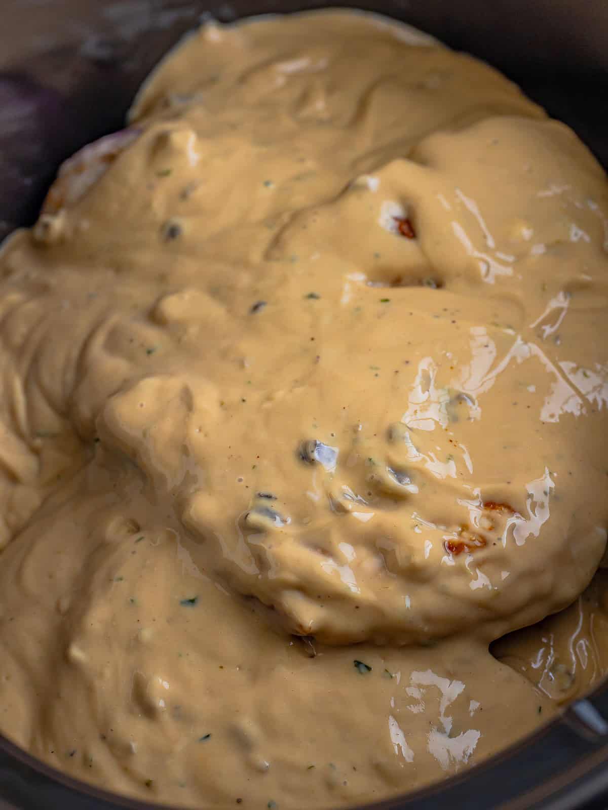 Creamy mushroom gravy poured over pork chops in the slow cooker before cooking.