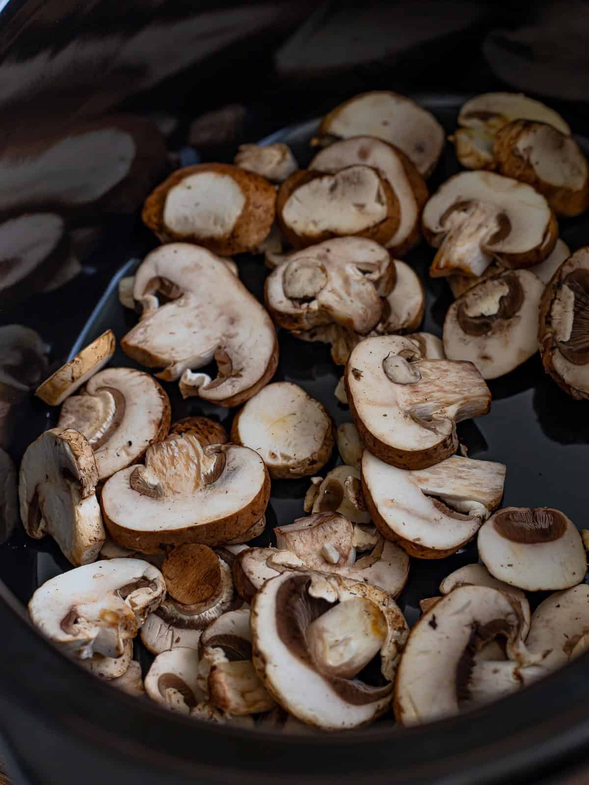 Sliced baby bella mushrooms spread in the bottom of a slow cooker.