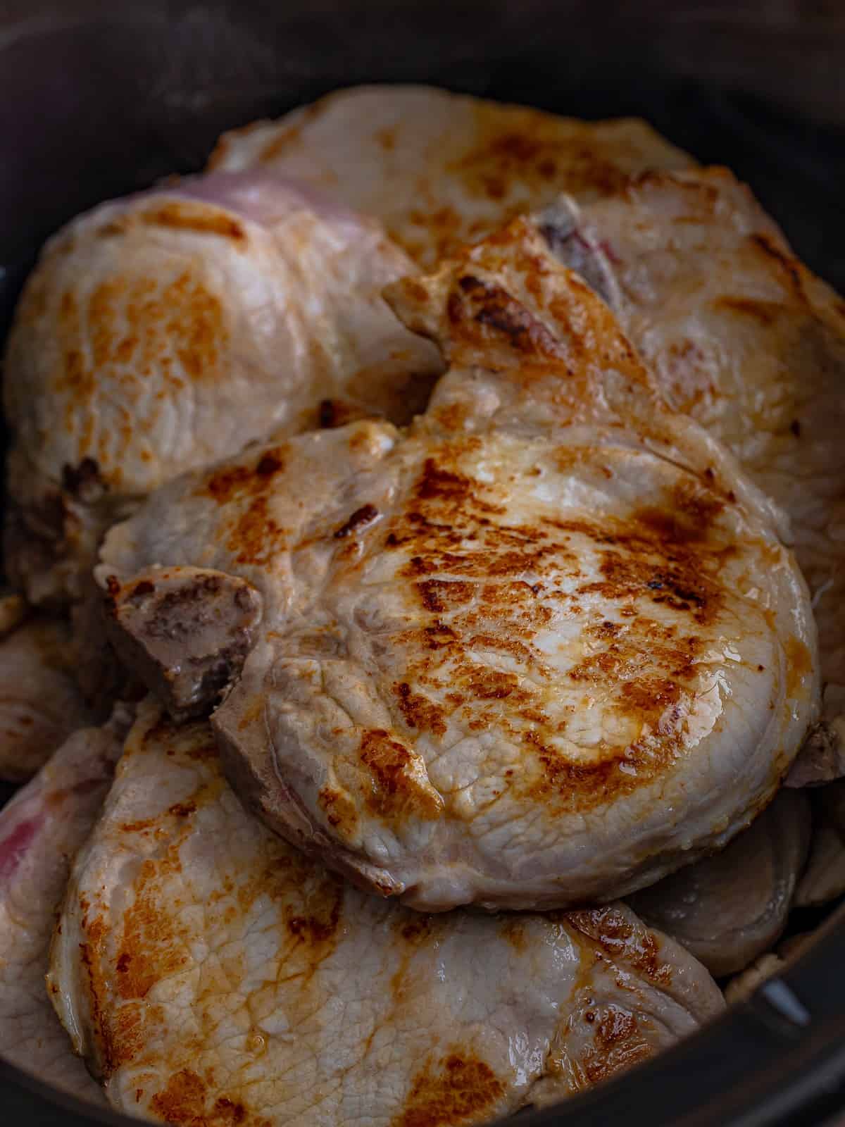 Golden seared bone in pork chops layered over mushrooms in a slow cooker.