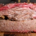 Thick slices of smoked brisket stacked on a cutting board showing a deep pink smoke ring and juicy bark.