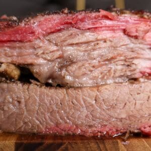 Thick slices of smoked brisket stacked on a cutting board showing a deep pink smoke ring and juicy bark.