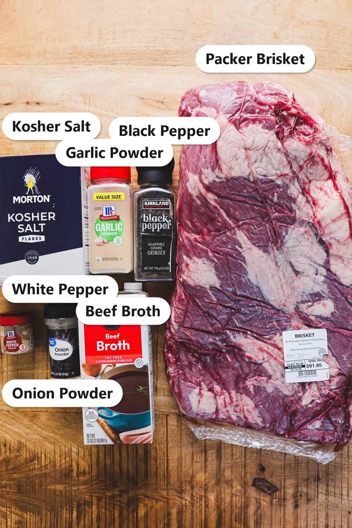 Labeled ingredients for smoked brisket including a whole packer brisket, kosher salt, black pepper, garlic powder, white pepper, onion powder, and beef broth.