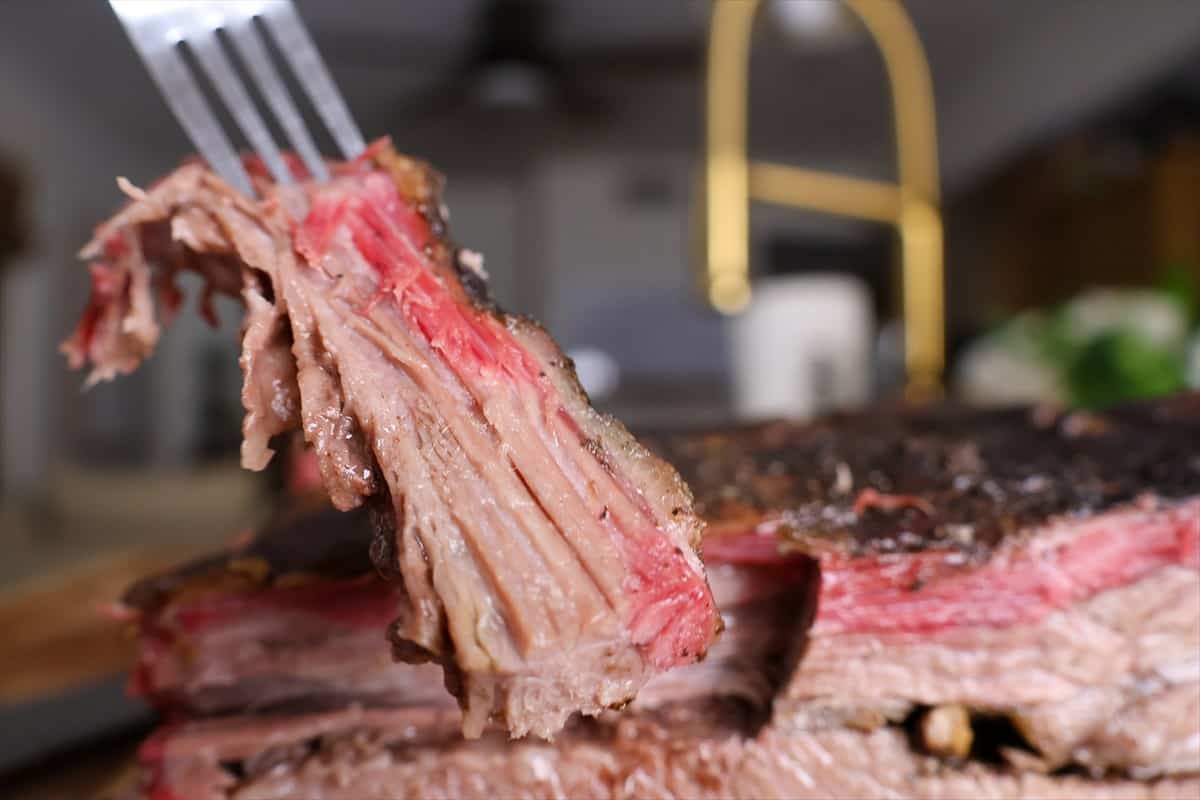 Fork holding up a tender slice of smoked brisket with a dark bark and pink smoke ring.