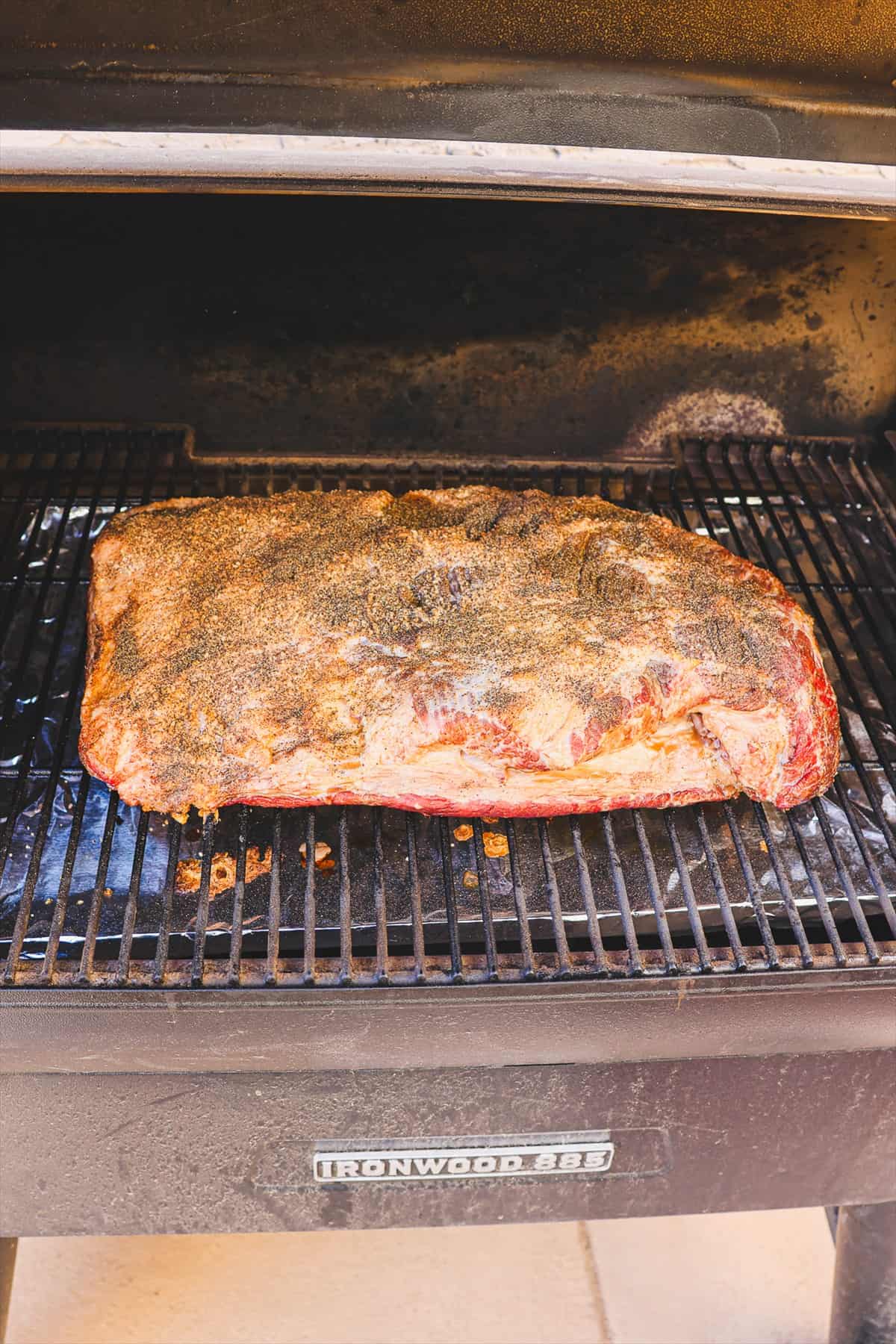 Seasoned brisket smoking fat side up on the pellet grill grates.