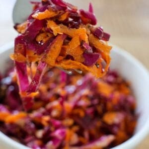 Forkful of vinegar coleslaw with shredded red cabbage and grated carrots lifted over a white bowl.
